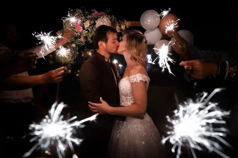 couple de mariés s'embrassant entouré de cierges magiques tenus par leurs invités dans l'obscurité