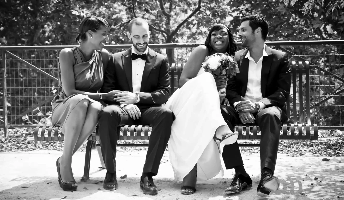 photo en noir et blanc d'un couple mixte assis sur un banc entouré d'un couple d'amis. Ils rigolent ensemble