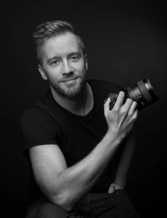 photo en noir et blanc du photographe Arnaud Loots, assis, tenant son appareil photo à la main