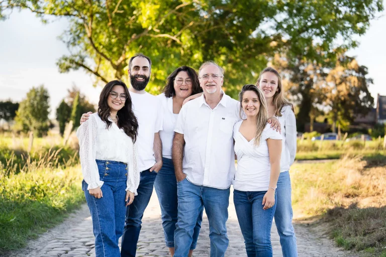 Photo d'une famille posant lors d'un shooting en extérieur près d'un champ. Ils sont tous habillés d'un pantalon en jean bleu et d'une chemise blanche