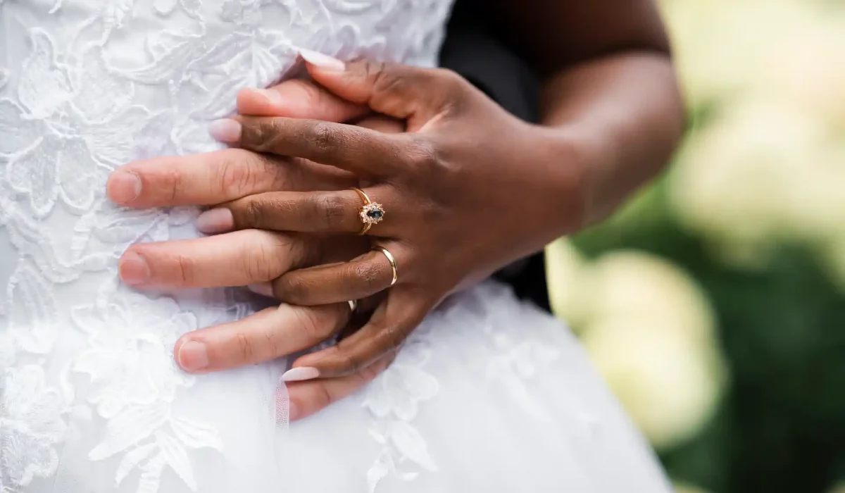 photo de mariage représentant les 2 mains enlacées des mariées sur la robe de la mariée. La bague est mise en valeur sur la main.