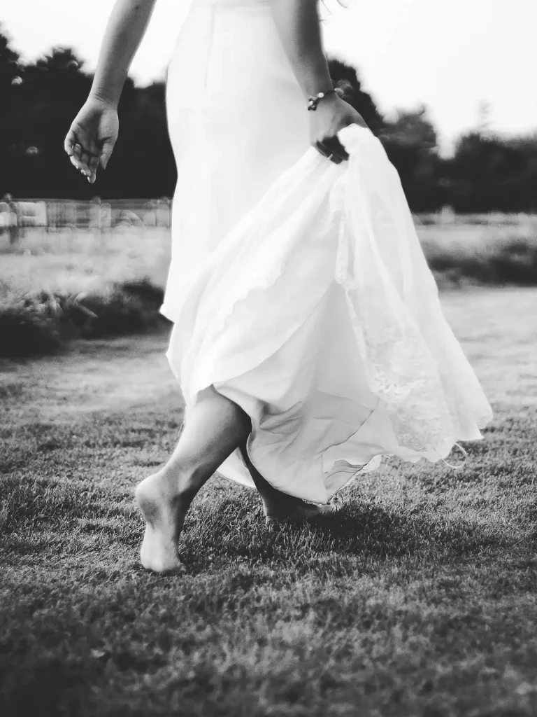 photo de mariage en noir et blanc cadrée sur le bas du corps de la mariée. La mariée marche pies nus dans l'herbe