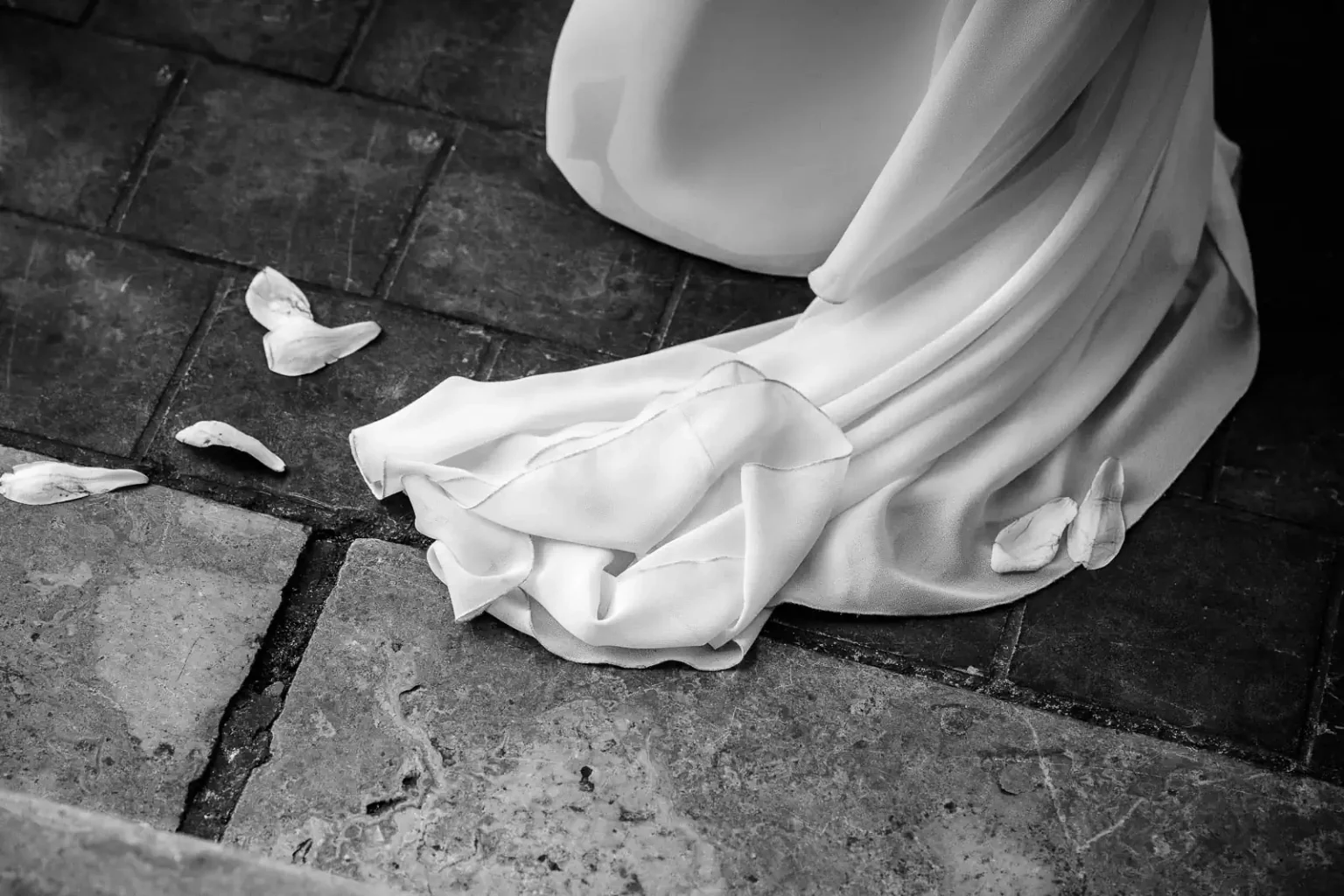 photo de mariage en noir et blanc montrant le bas de la robe de mariée avec quelques pétales de fleurs sur le sol