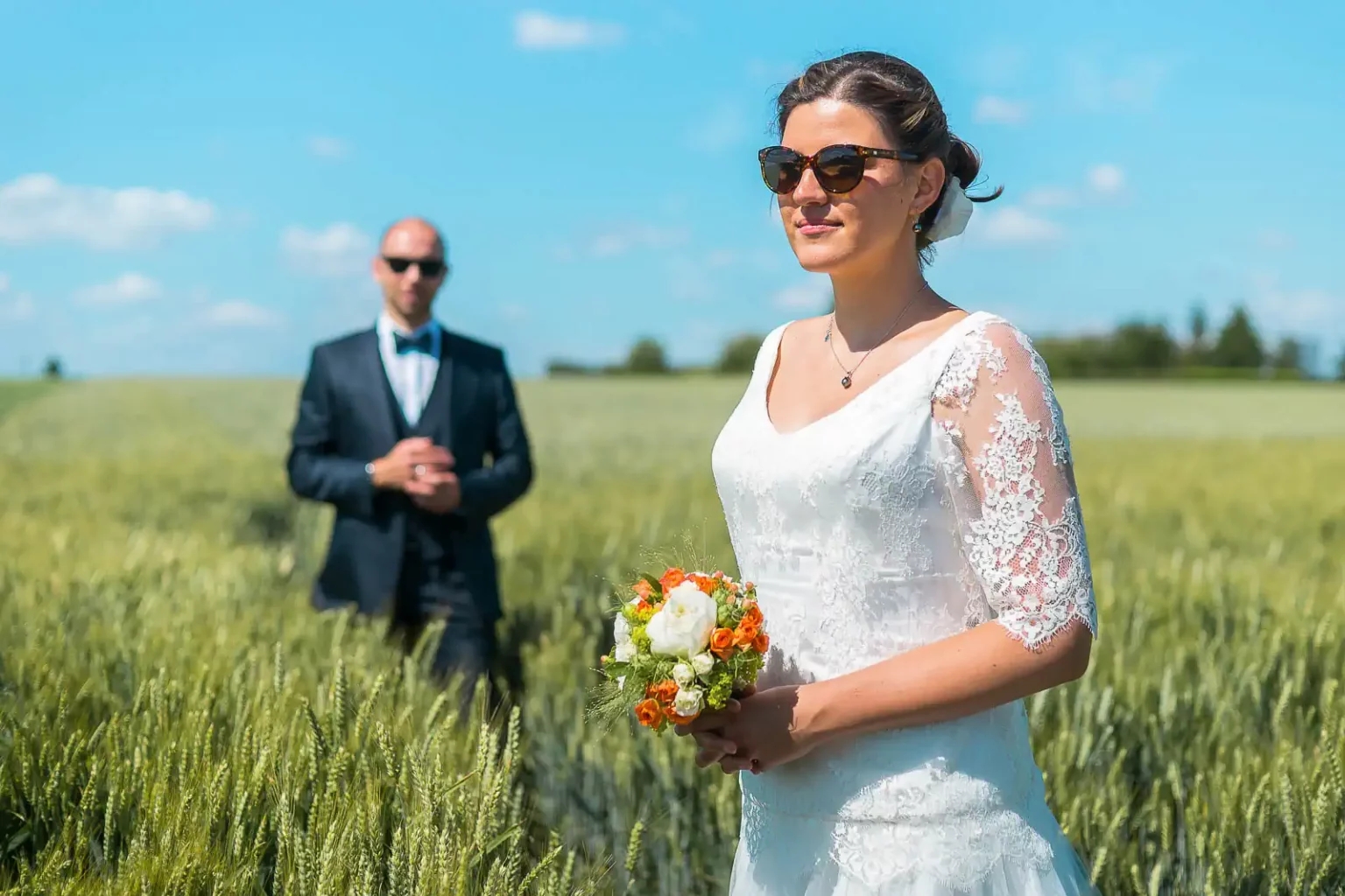 photo de mariage prise dans un champ près de Lille. Les mariés portent des lunettes de soleil et la marié tient un bouquet de fleurs dans ses mains