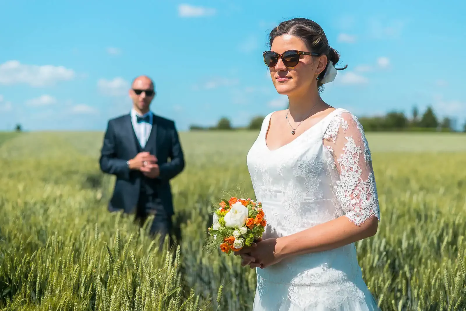 photo de mariage prise dans un champ près de Lille. Les mariés portent des lunettes de soleil et la marié tient un bouquet de fleurs dans ses mains
