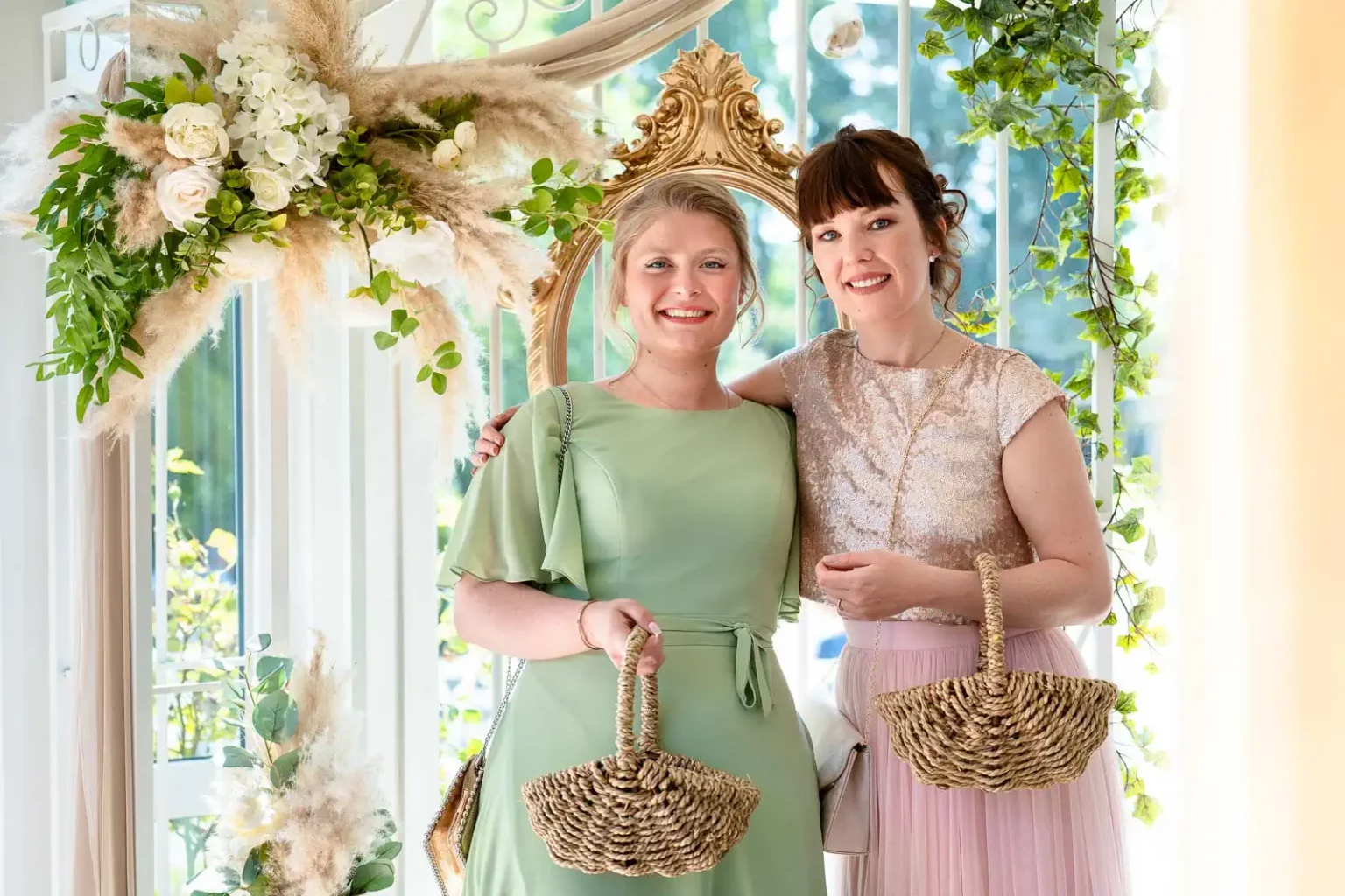 photo de 2 demoiselles d'honneur posant devant une décoration florale de mariage en portant chacune un panier en osier