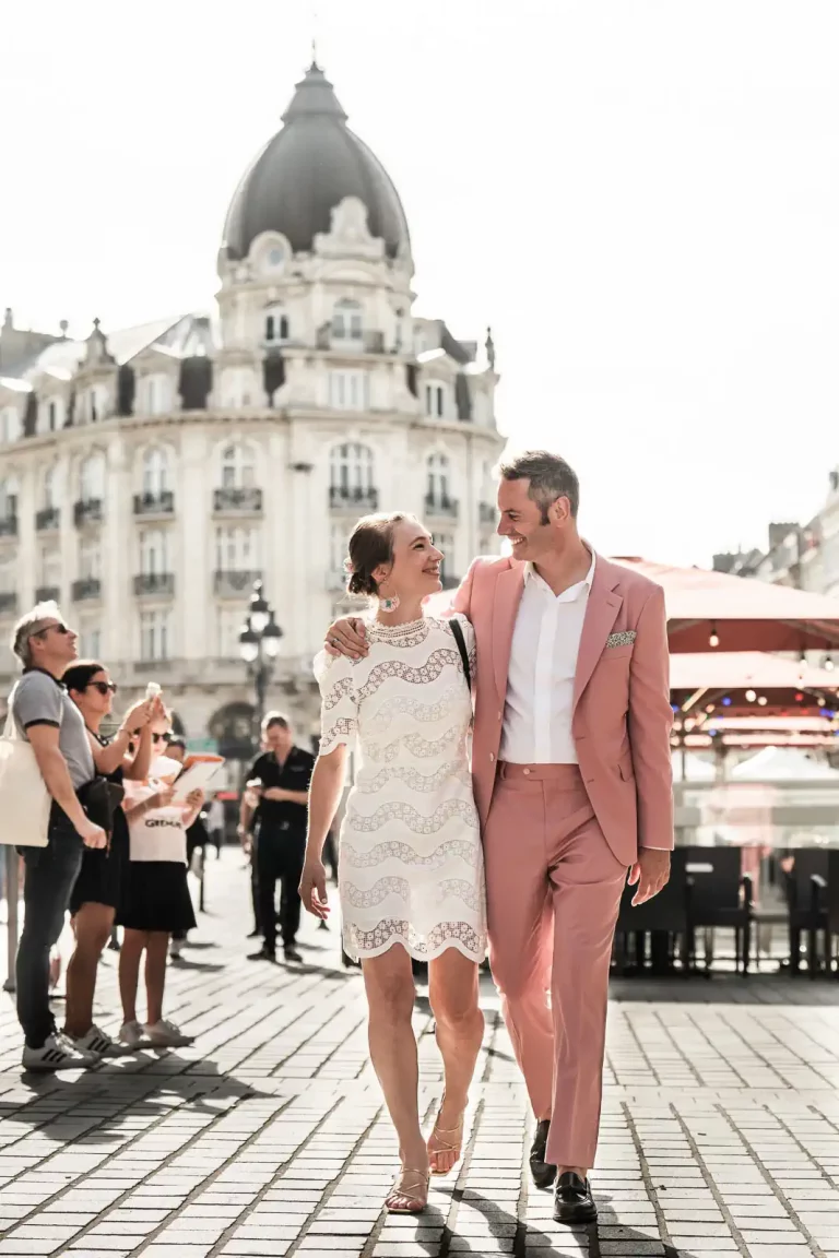 photo mariage d'un couple de mariés habillé en rose et blanc, marchant devant l'hôtel Carlton à Lille
