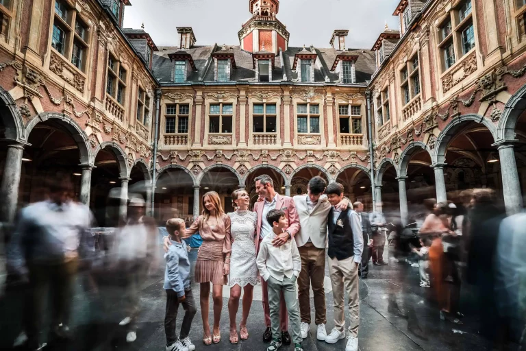 Couple de mariés et leurs enfants posant dans la cour intéreur de la Vieille Bourse à Lille. La photo est prise en pose longue, la famille est nette tandis que les passants sont flous.