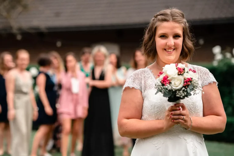 photo de mariage d'une mariée tenant un bouquet de fleur qu'elle s'apprête à lancer dans les airs. Ses amies et demoiselles d'honneur attendent derrière elle qu'elle le lance