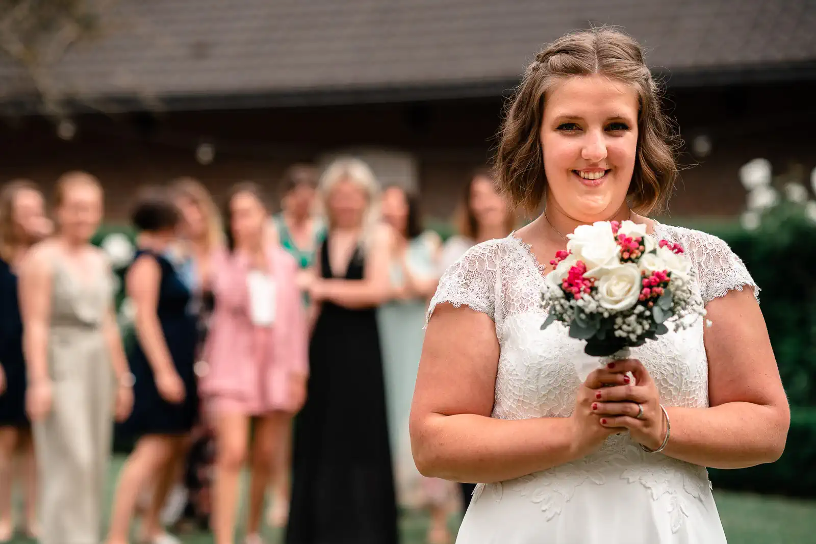 photo de mariage d'une mariée tenant un bouquet de fleur qu'elle s'apprête à lancer dans les airs. Ses amies et demoiselles d'honneur attendent derrière elle qu'elle le lance
